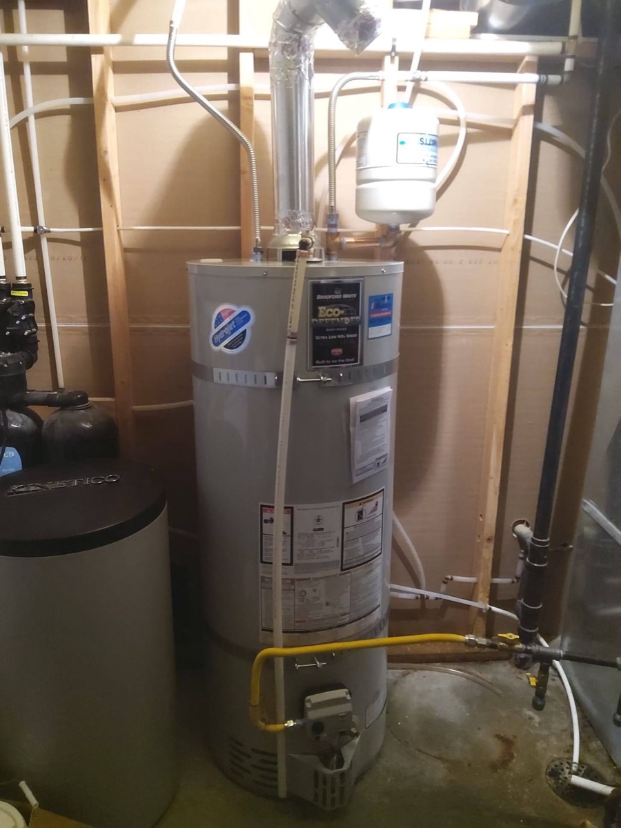 Water heater in a utility closet with pipes, valves and a yellow gas line (site alt text)