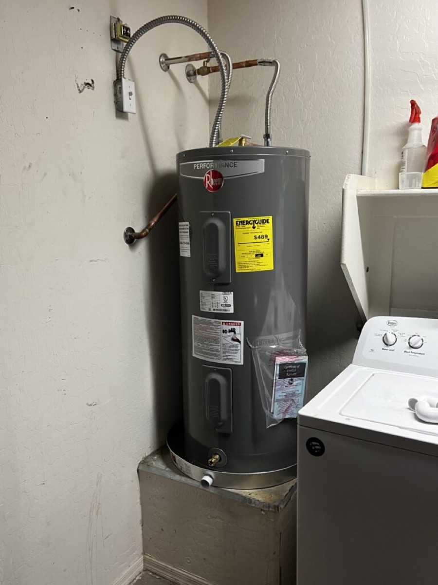 Newly installed Rheem electric tank water heater on a stand in a laundry area
