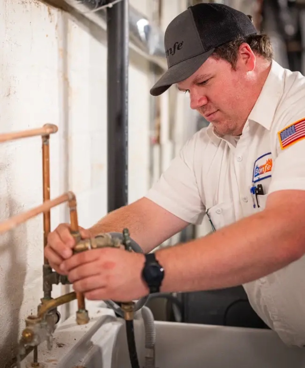 Bonfe plumber in branded uniform working on basement copper piping