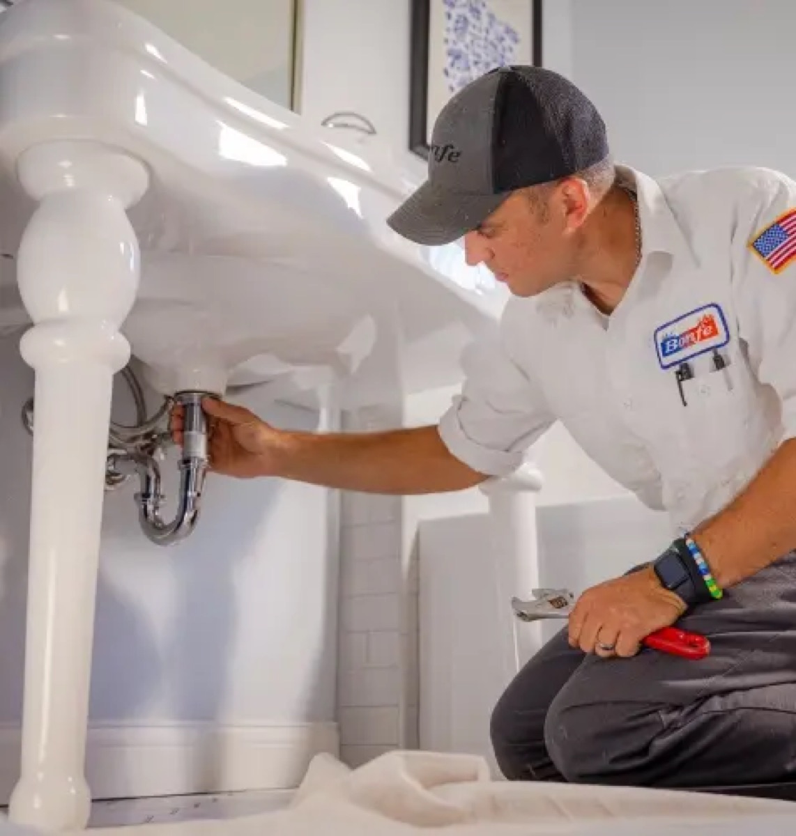Bonfe plumber in branded uniform working under a pedestal sink