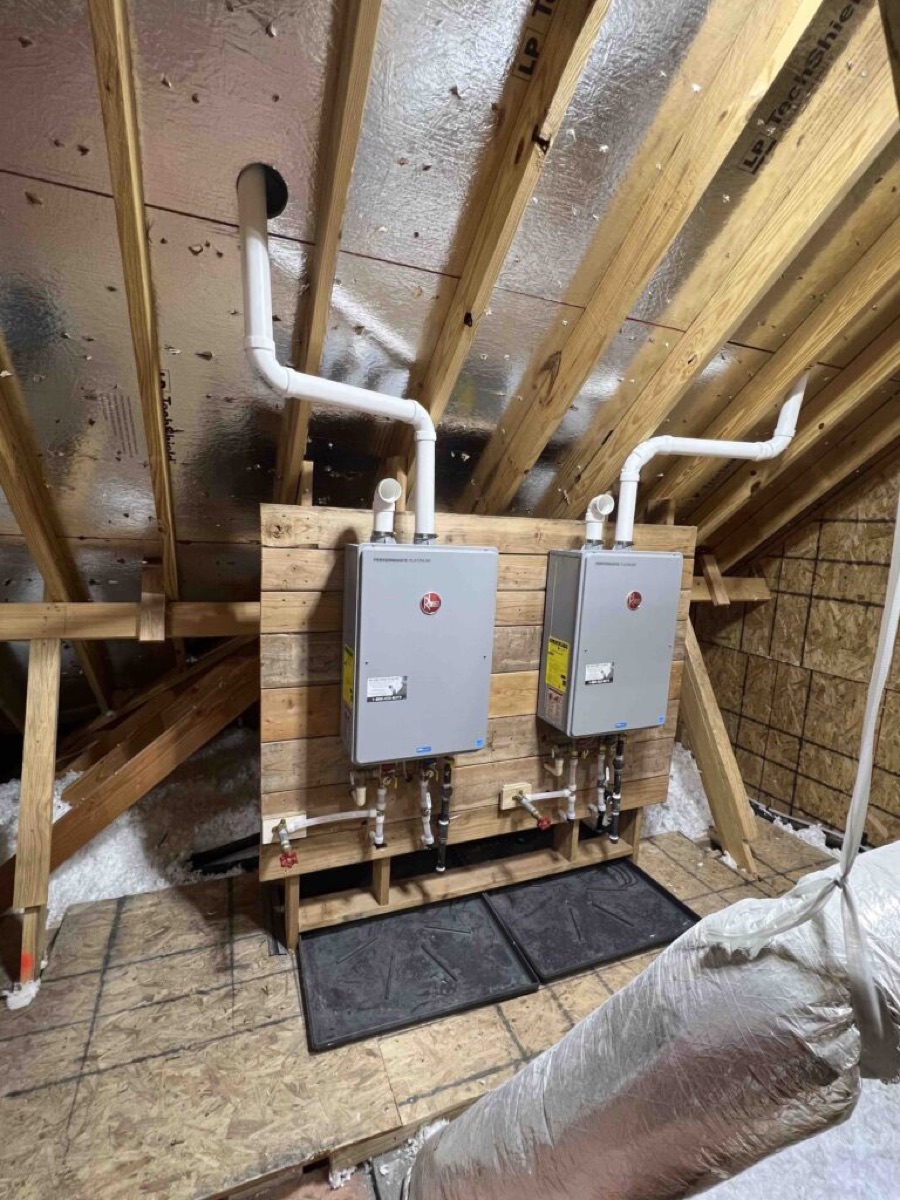 Two tankless water heaters mounted on a board in an attic