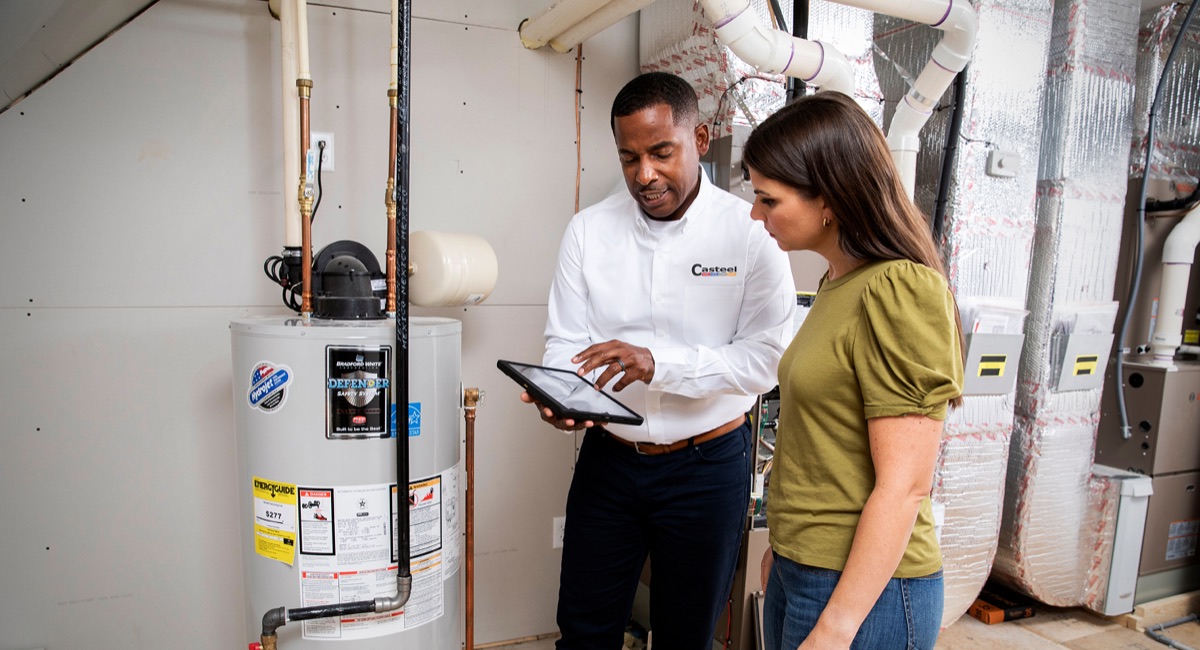 Casteel technician and homeowner reviewing a tablet next to a water heater