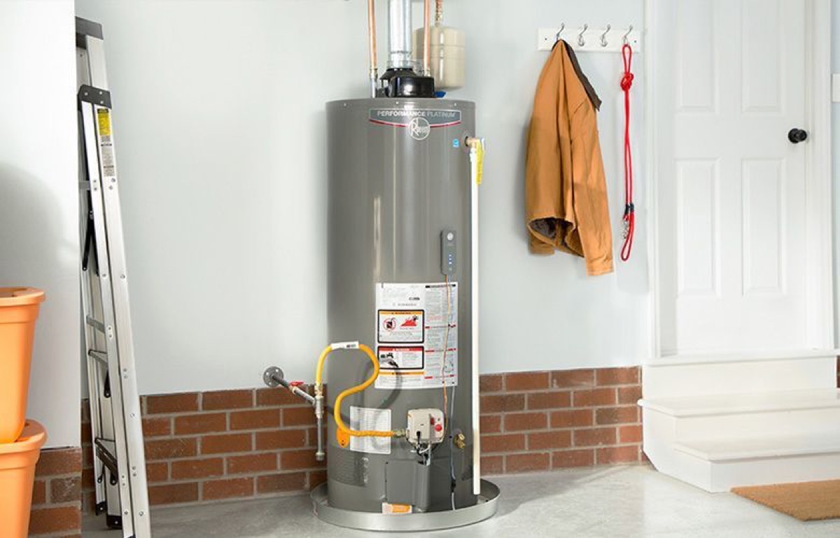 Gray tank water heater installed in a basement with brick wall