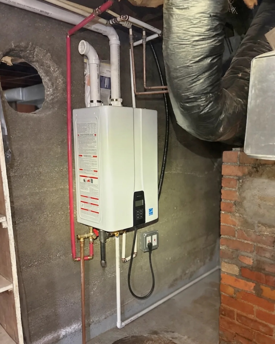 Finished tankless water heater on a basement wall with PVC venting, supply lines and isolation valves