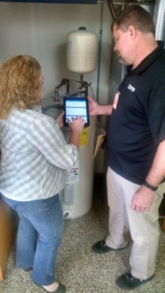 DRF technician reviewing options with a homeowner beside an installed electric tank water heater and expansion tank (site alt: 'Water Heater Replacement from DRF')