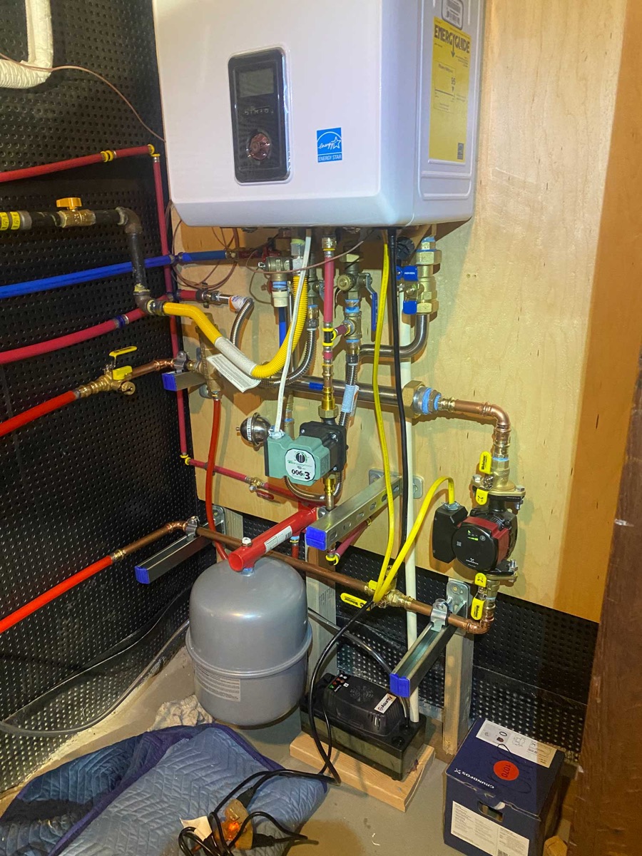 Wall-mounted tankless water heater installation with piping and expansion tank