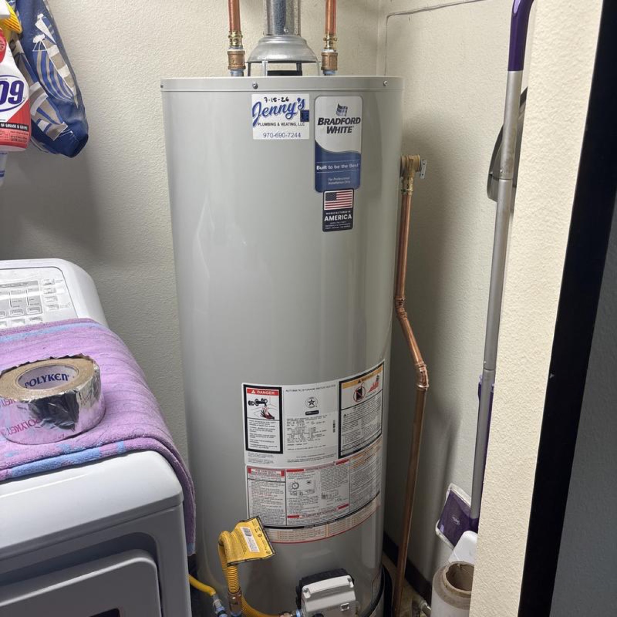Bradford White tank water heater with new copper piping and Jenny's sticker, installed in a laundry area