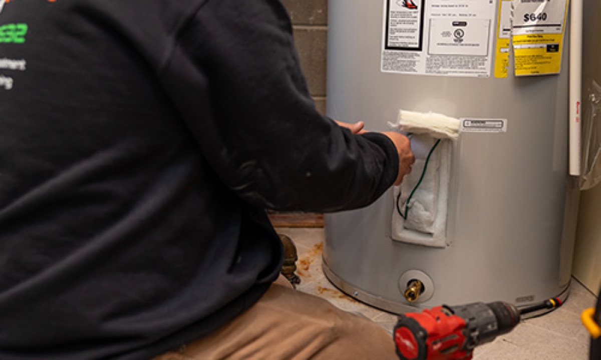 Modern Plumbing technician in branded hoodie working on an electric tank water heater
