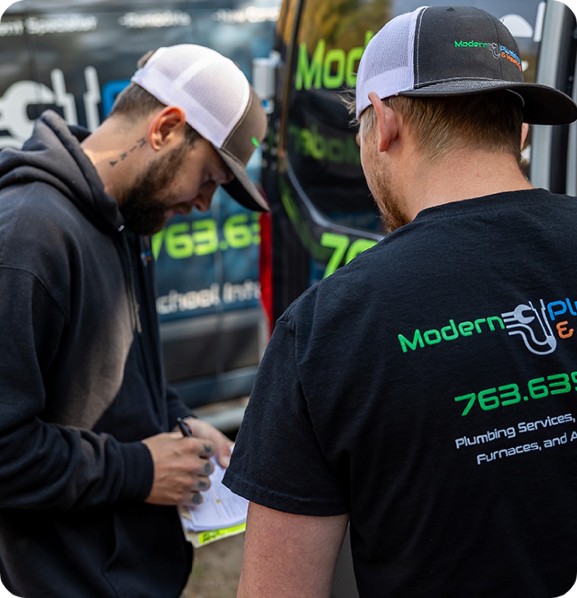 Modern technicians in branded shirts reviewing paperwork beside a company van