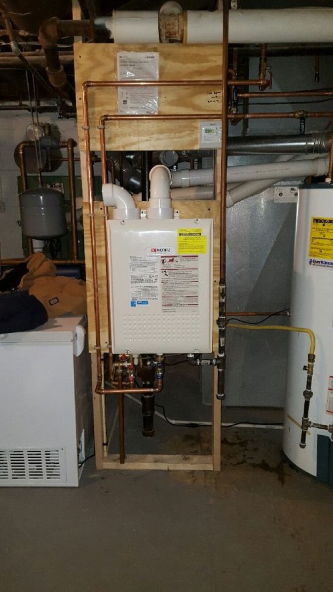 Noritz tankless water heater mounted on a plywood backer board in a basement