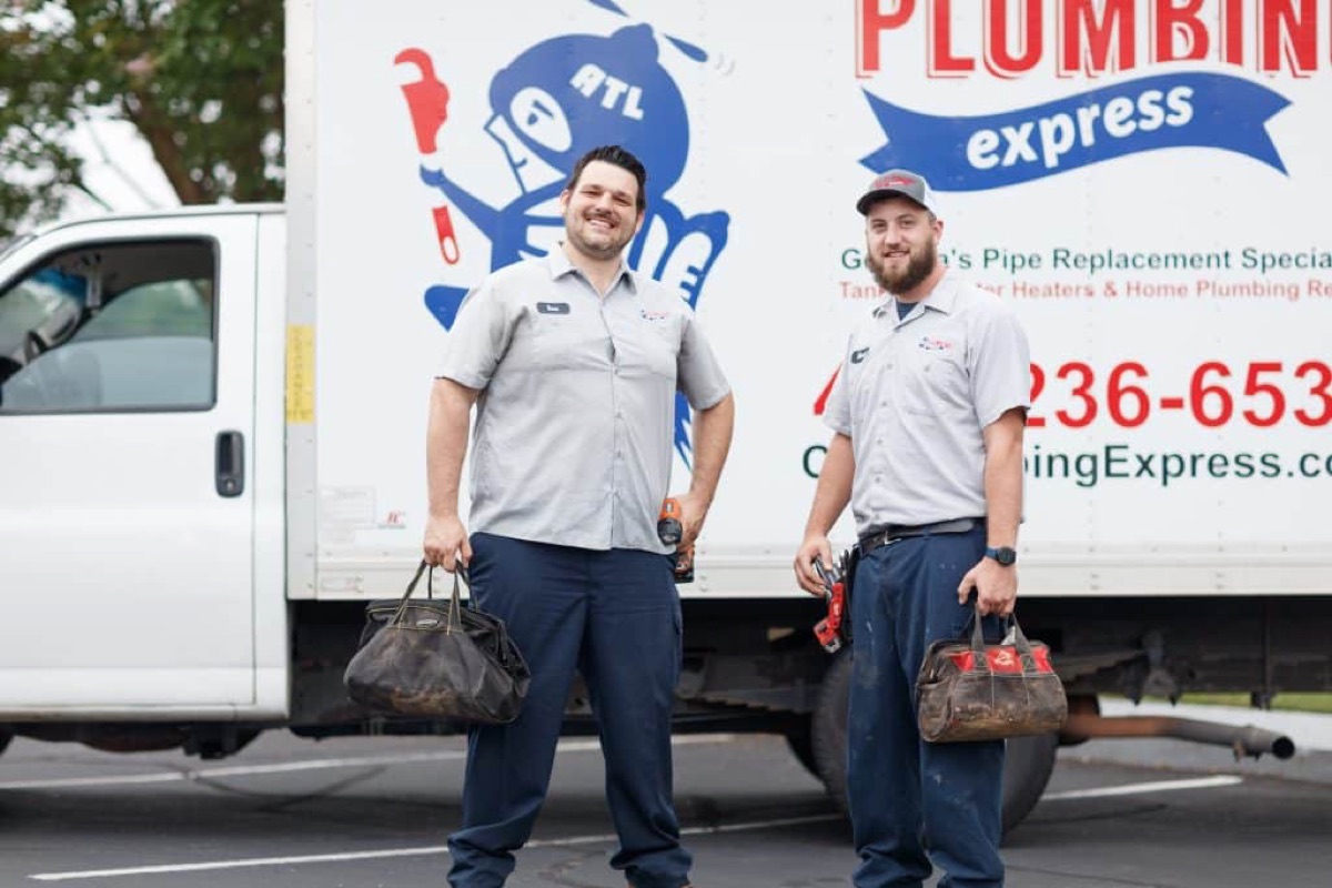 Two Plumbing Express technicians with tool bags in front of a branded service truck