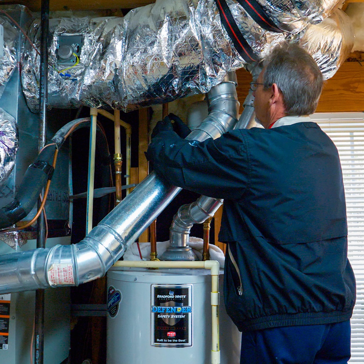 Technician servicing a Bradford White Defender water heater with venting
