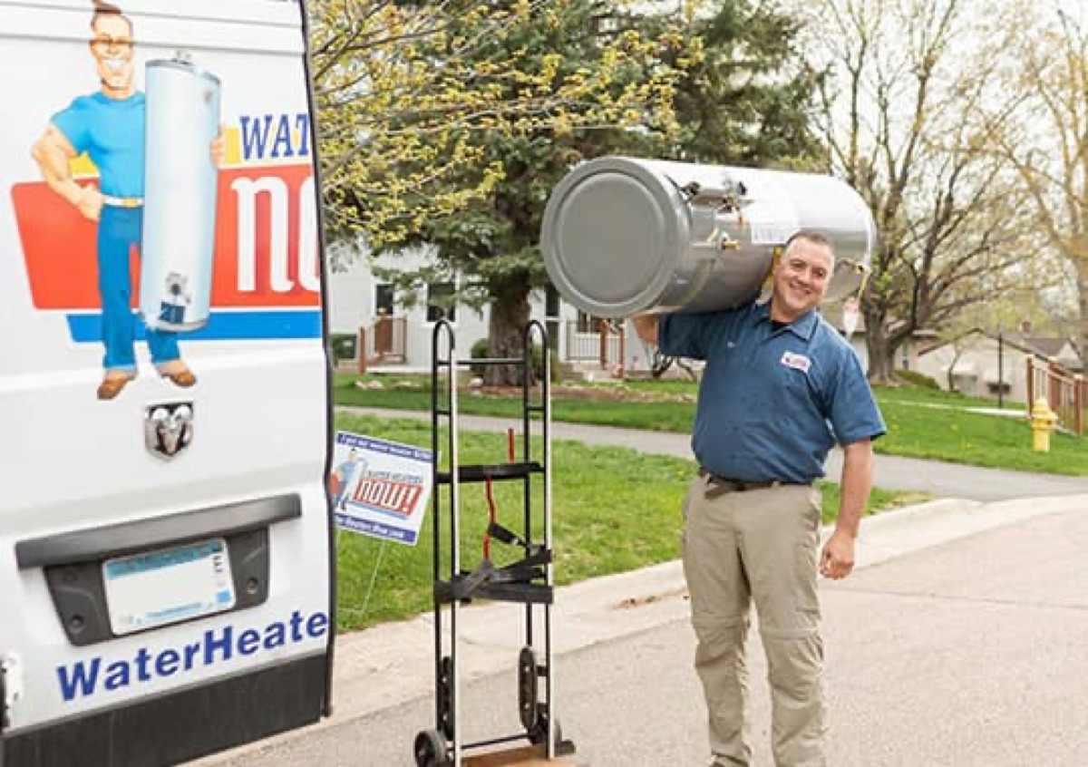 Water Heaters Now installer carrying a new tank water heater past the branded van