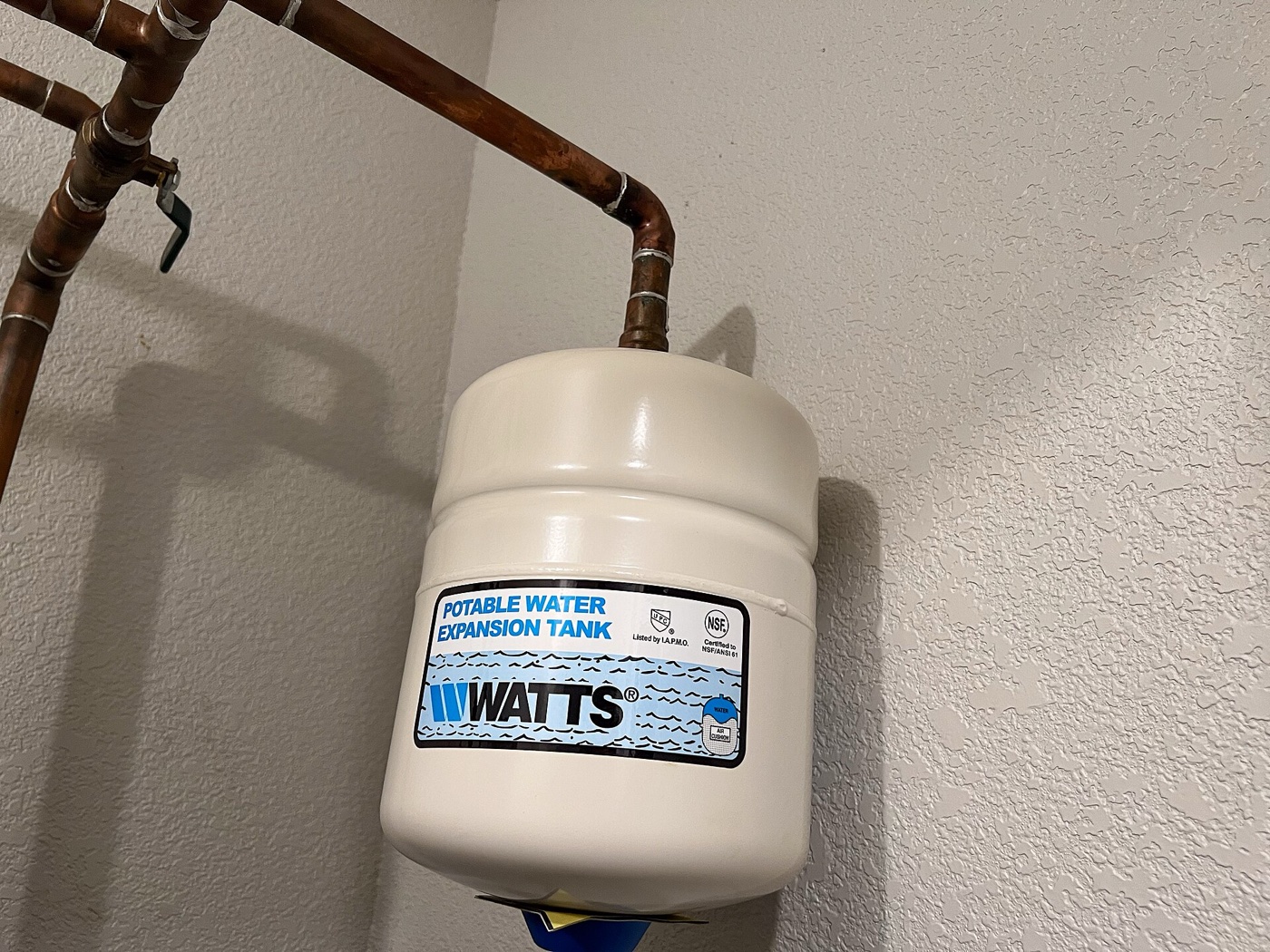 White potable water thermal expansion tank hanging from a copper pipe