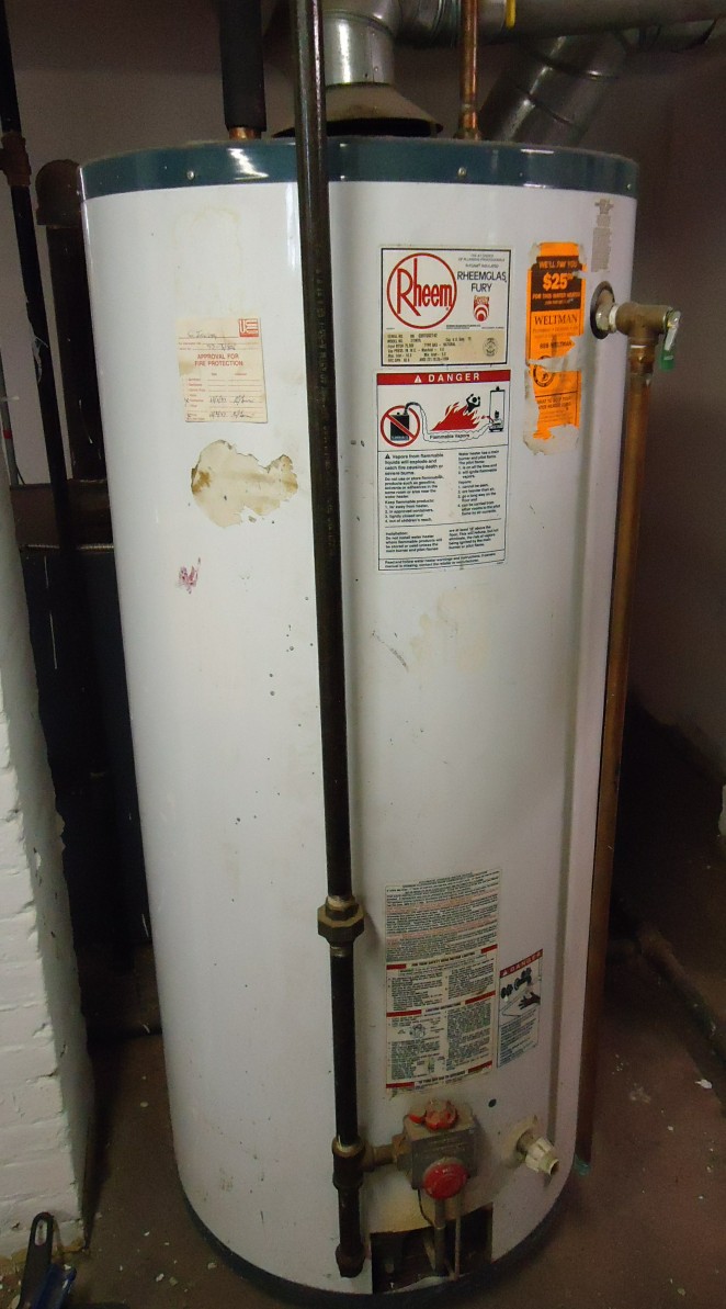 Tall white gas-fired tank water heater with pipes in a home basement