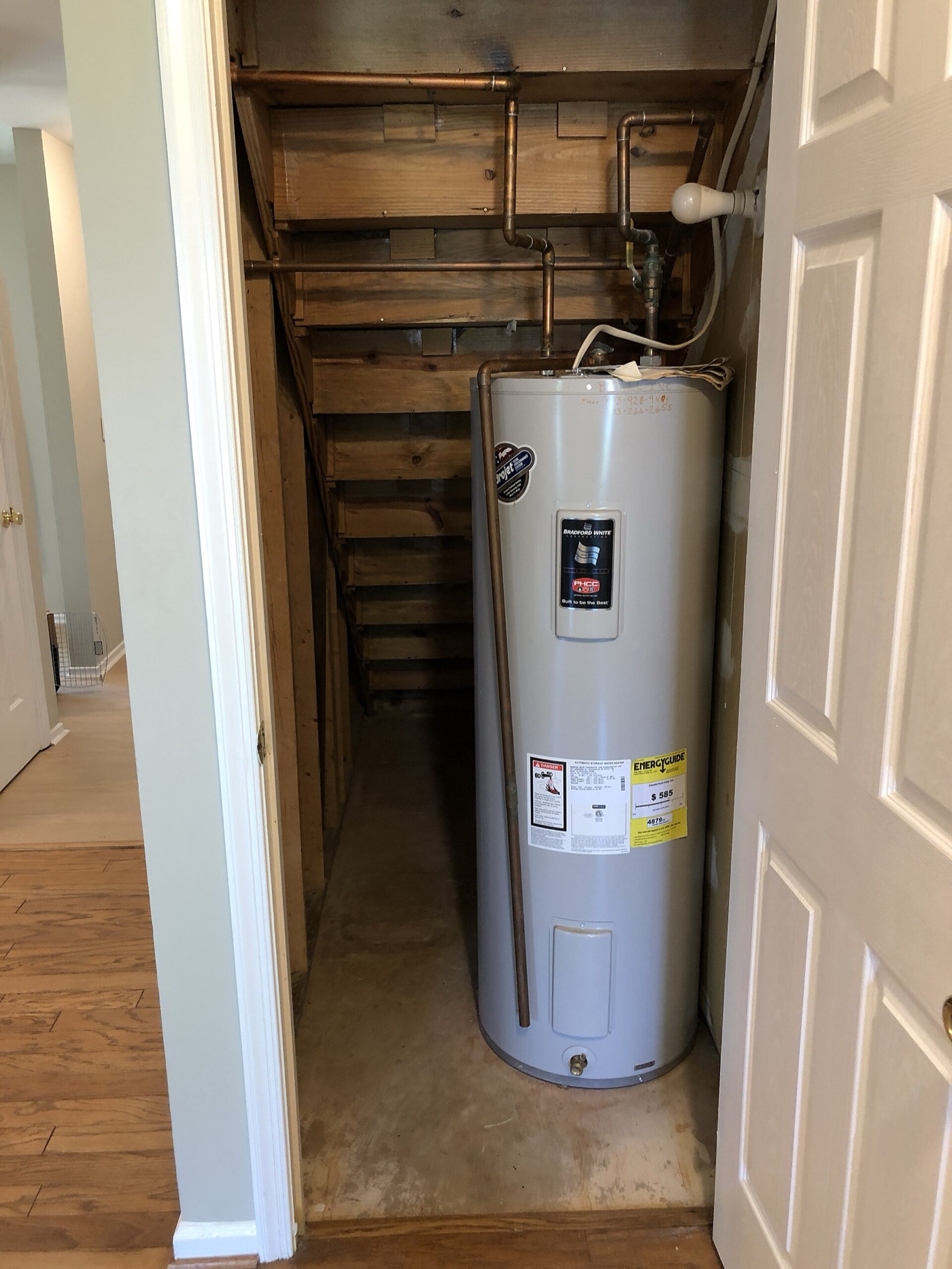 Tank water heater standing in a narrow utility closet under the stairs