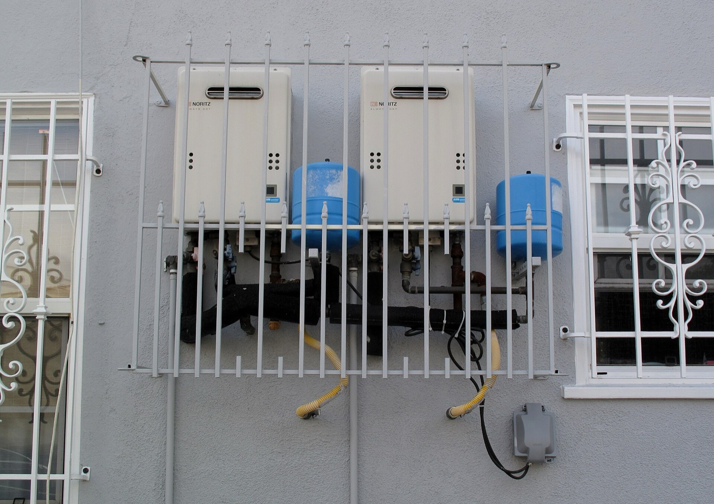 Two wall-mounted gas tankless water heaters with piping on an exterior wall