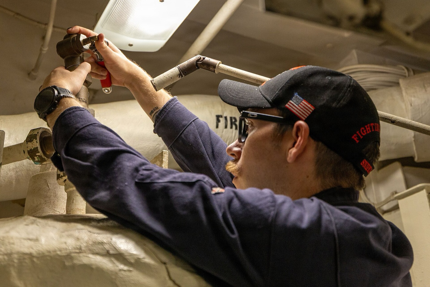 Technician working on the relief valve at the top of a hot water booster heater aboard a ship