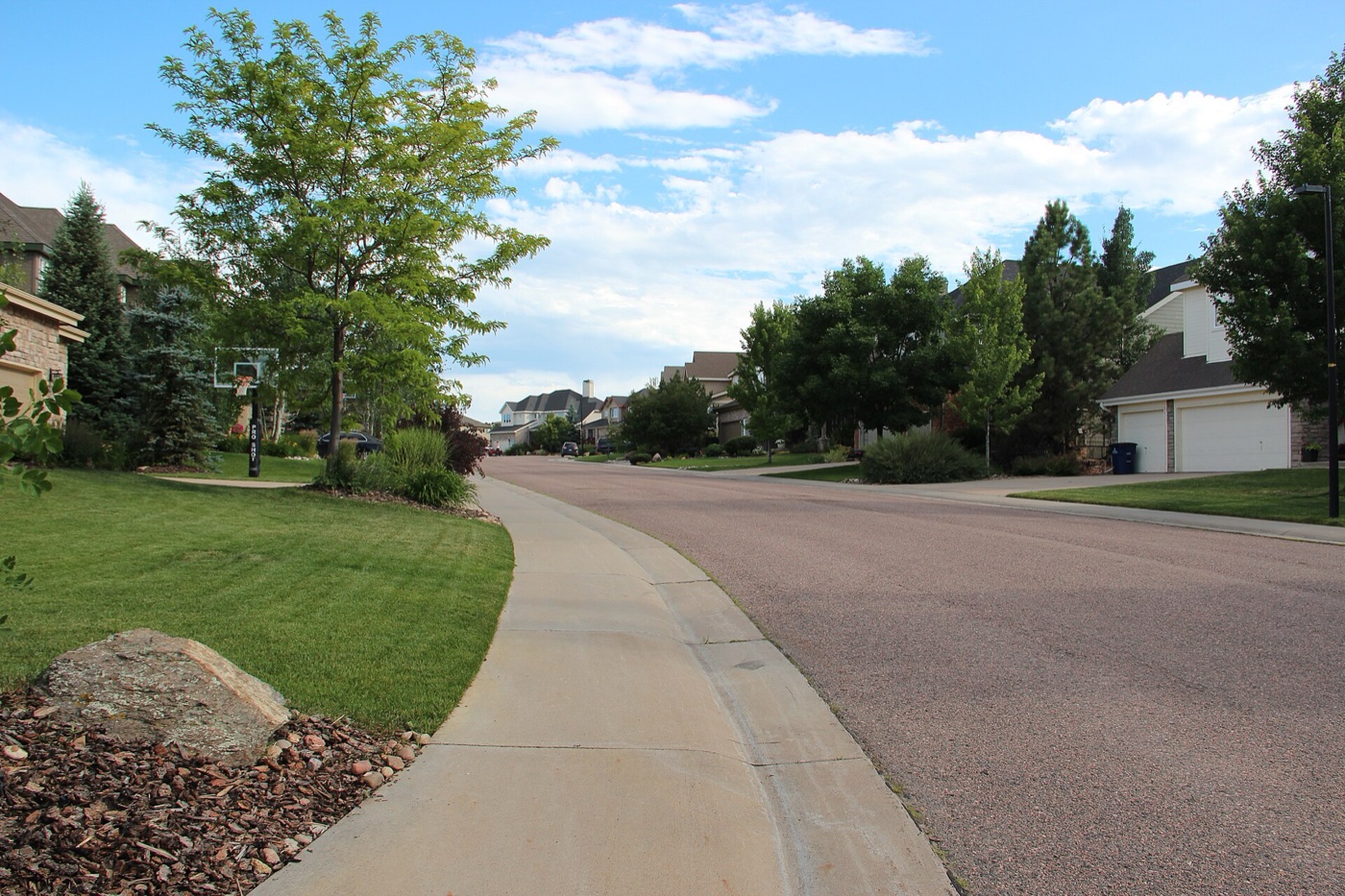 Curving residential street with sidewalk, lawns and houses in a Castle Pines neighborhood