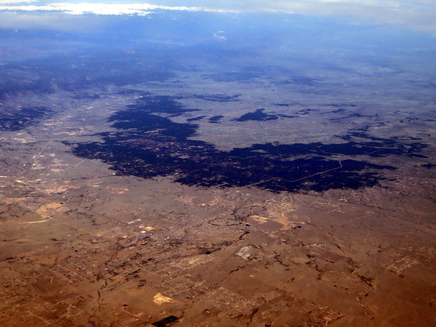 Aerial view of the dark ponderosa pine forest of Black Forest surrounded by open plains northeast of Colorado Springs
