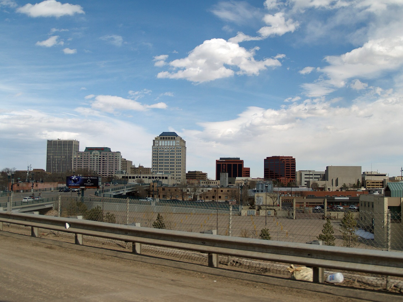 Downtown Colorado Springs office towers seen from a highway overpass under a partly cloudy sky