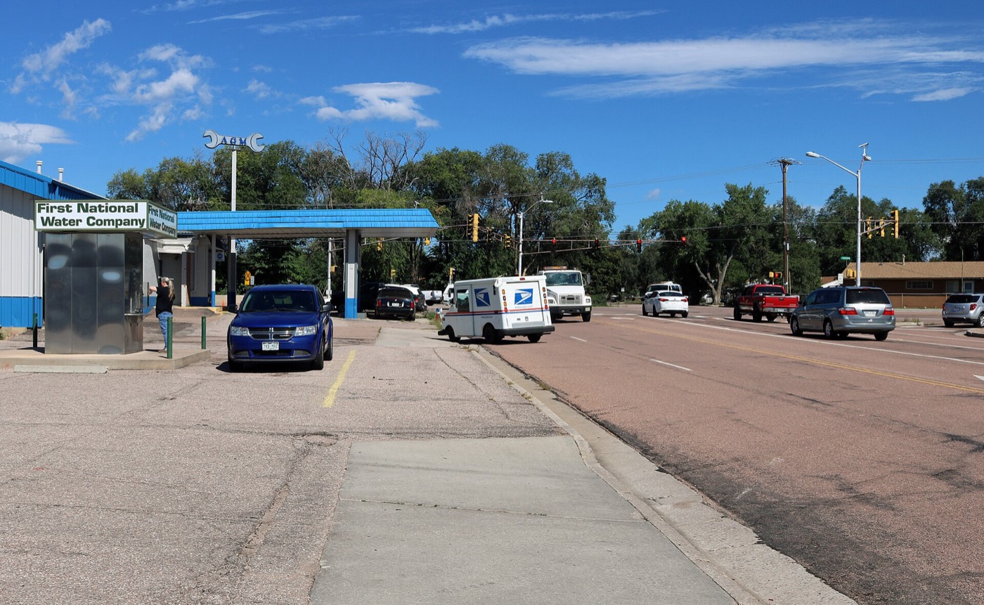 Looking northwest along Widefield Boulevard toward the Fontaine Boulevard traffic light, with a water vending kiosk and a mail truck
