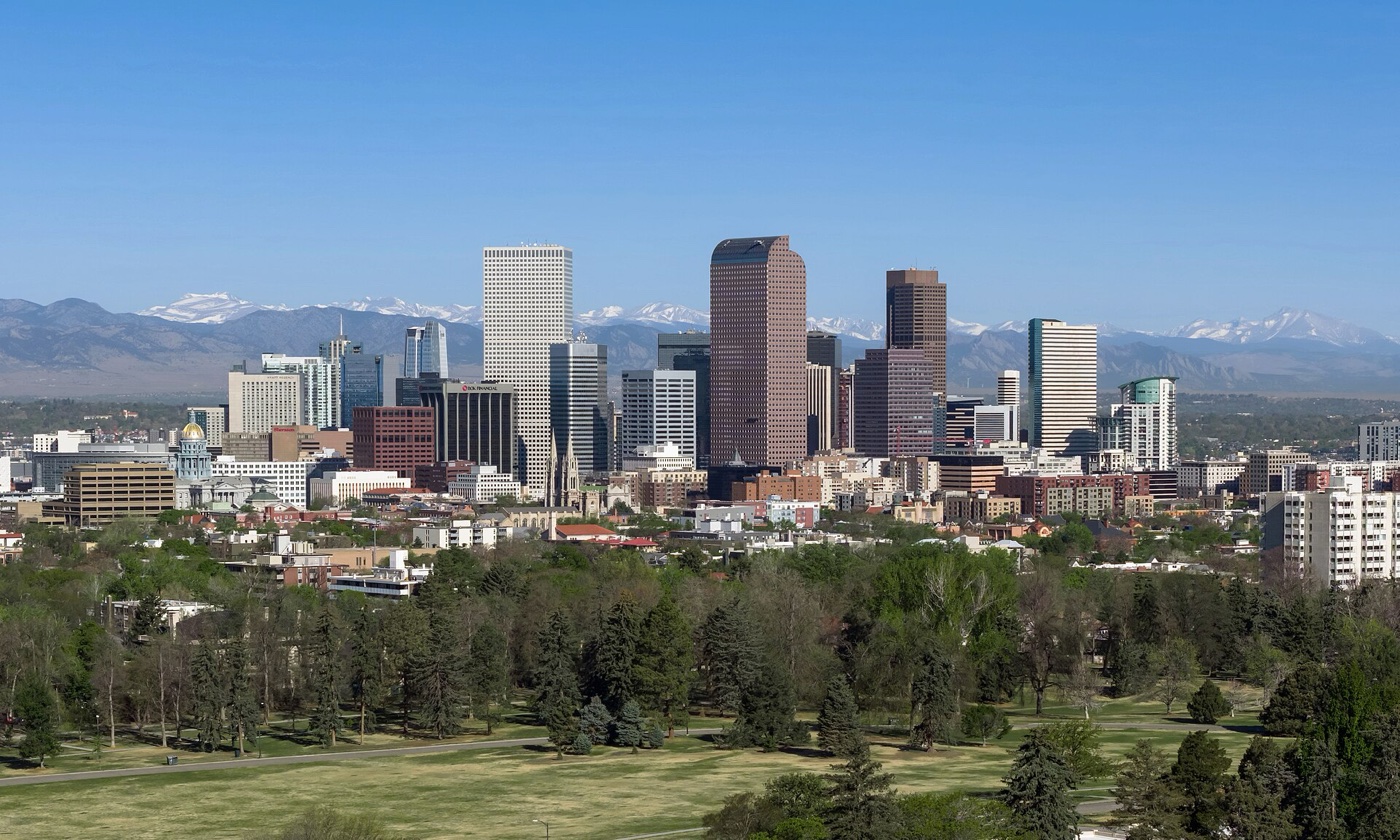 Downtown Denver high-rises rising above green trees with snow-capped Rocky Mountains on the horizon