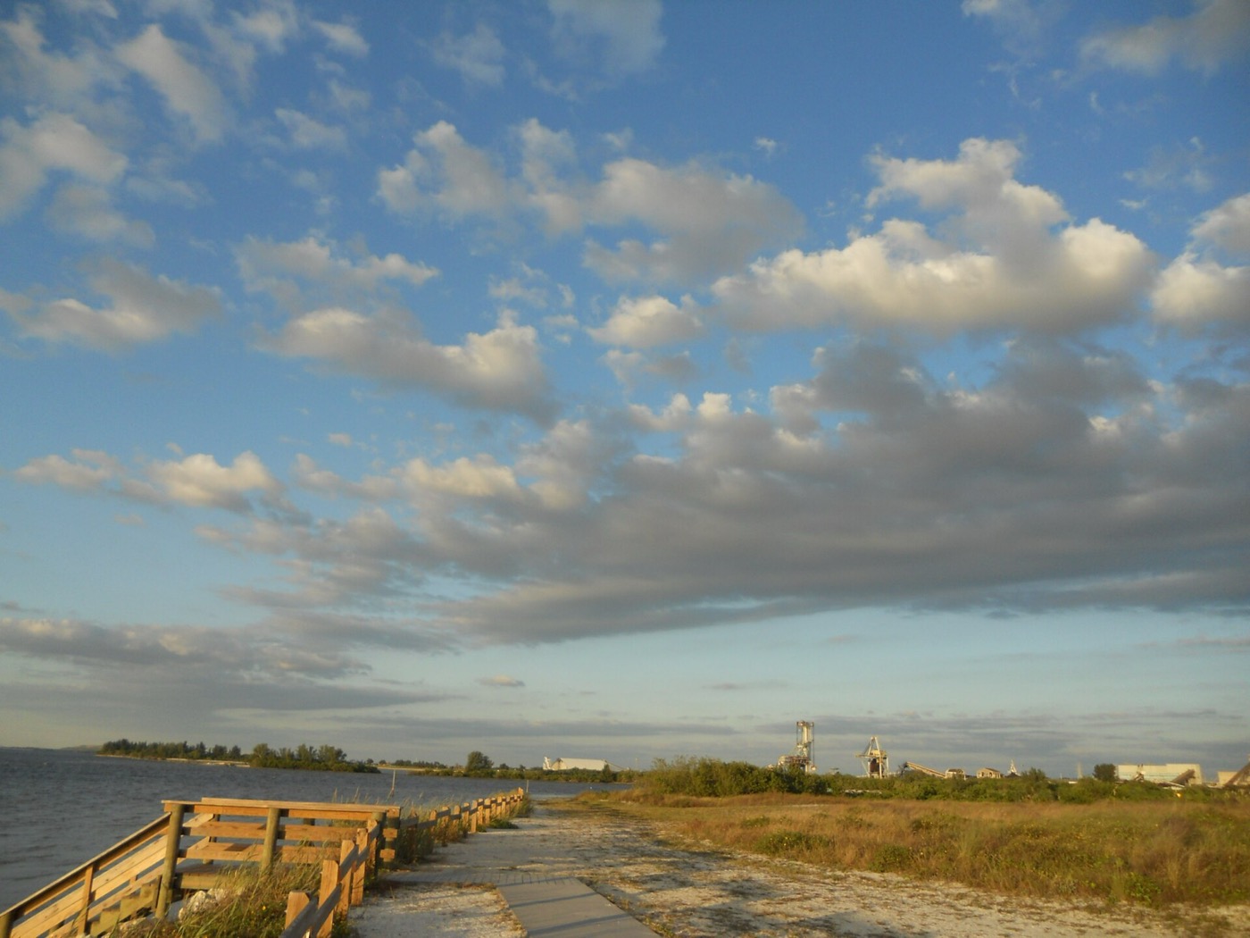 A wooden boardwalk and path along the Tampa Bay shoreline at Apollo Beach under a partly cloudy sky