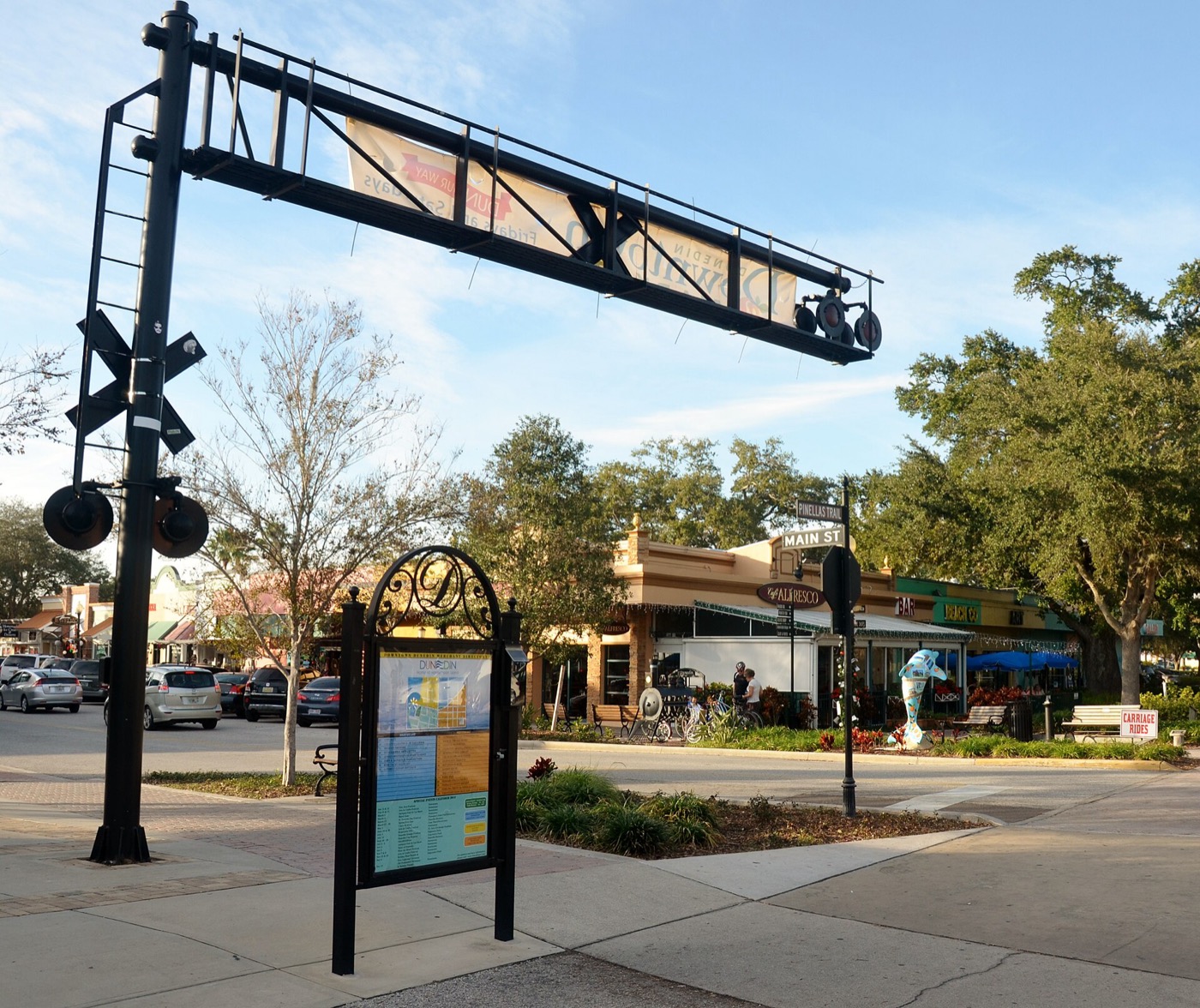 Downtown Dunedin street corner with the railroad-crossing style gateway arch, shops and palm trees