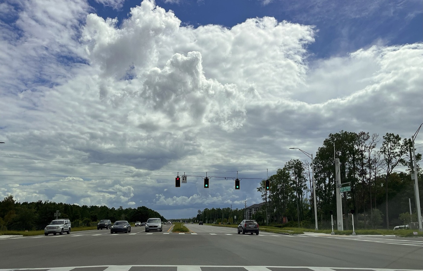 A wide multi-lane road intersection with traffic signals under a cloudy sky in Wesley Chapel, Florida
