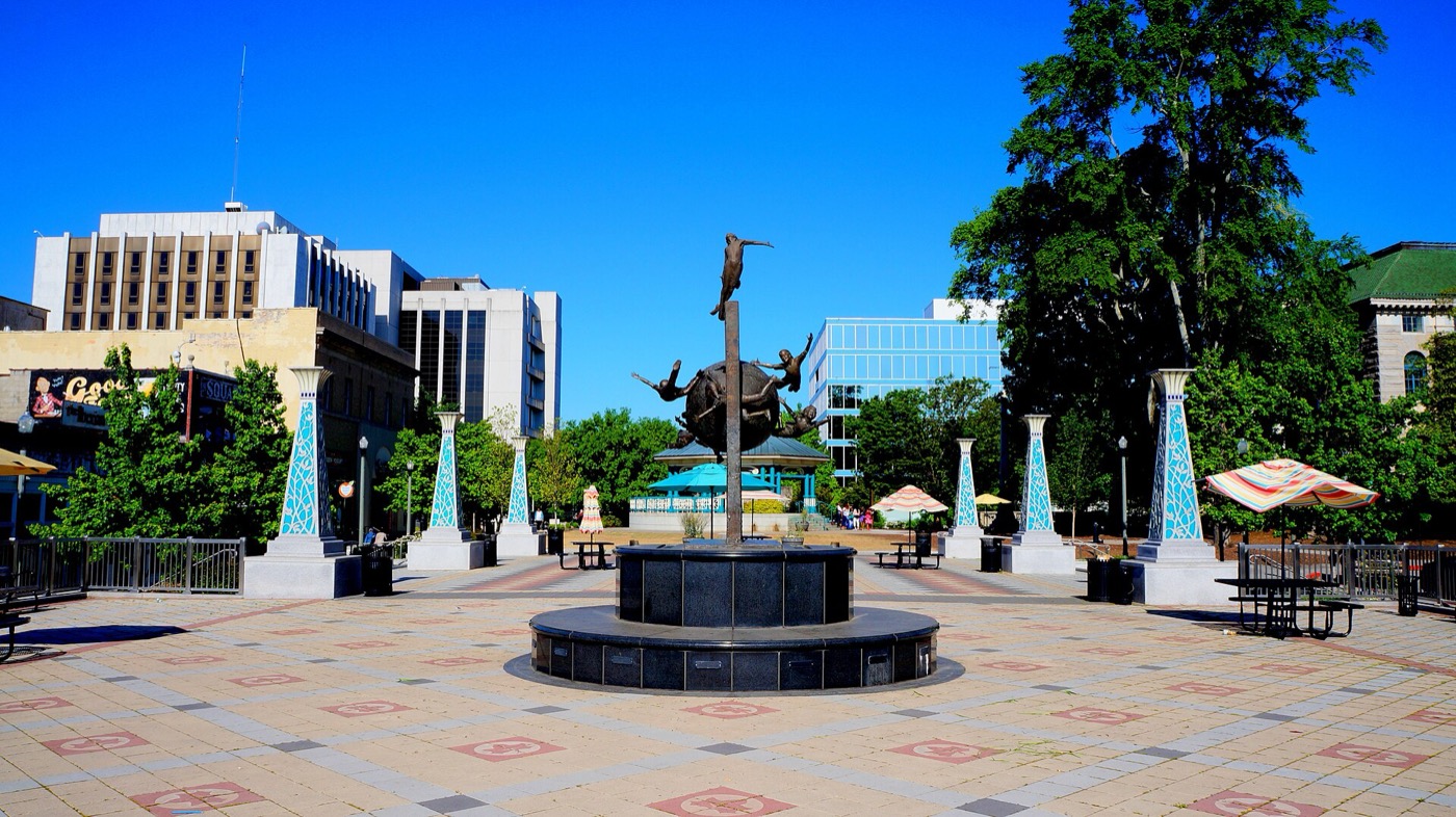 Brick plaza on Decatur Square with a central sculpture, tiled pillars and downtown buildings