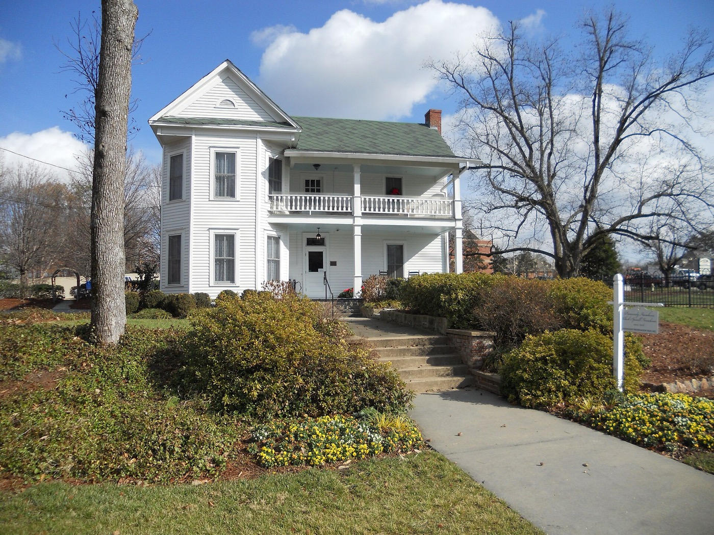 White two-story Dunwoody Farmhouse with a double front porch, shrubs and a walkway