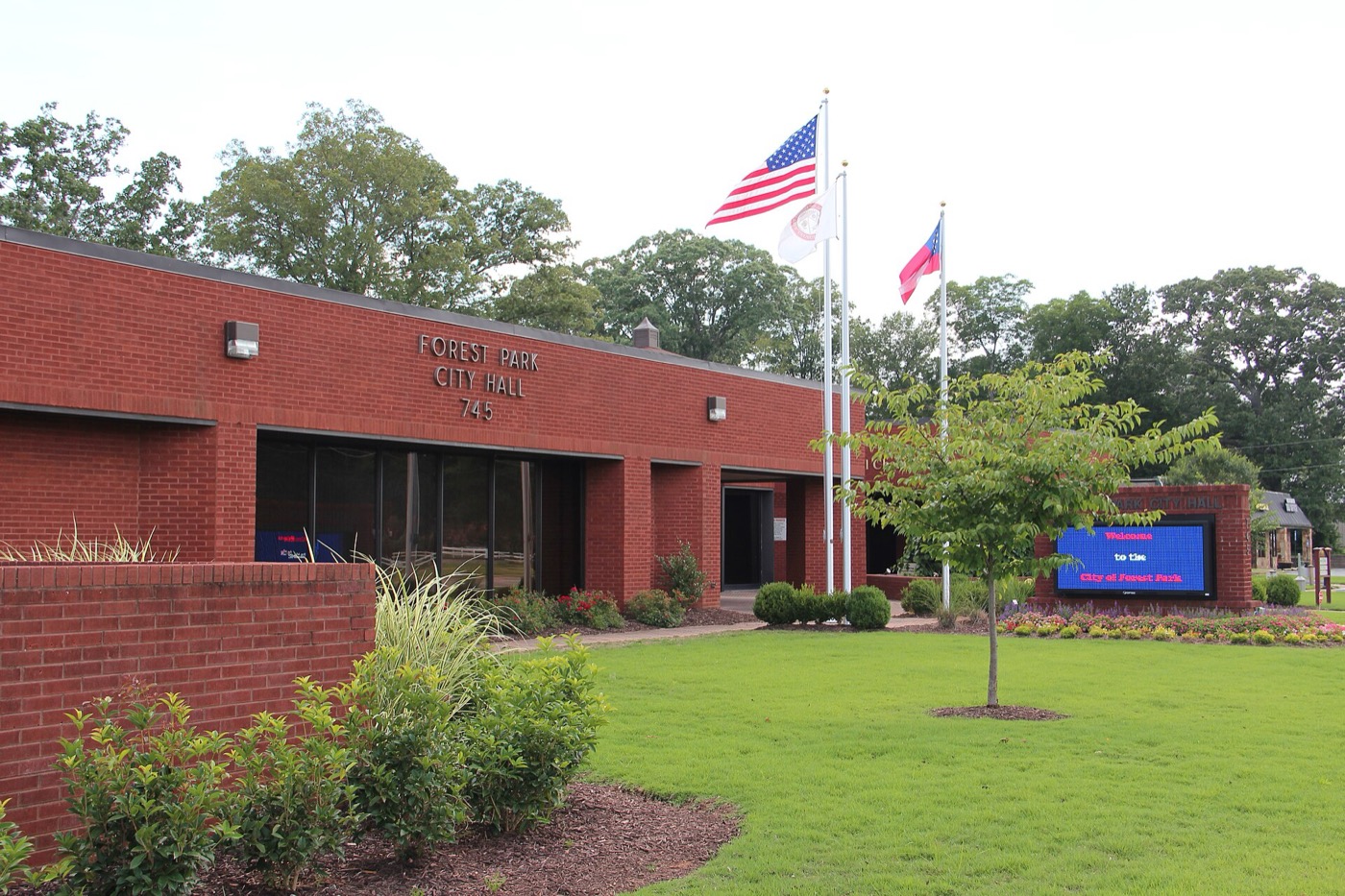 Low red-brick Forest Park City Hall with flagpoles and a landscaped lawn