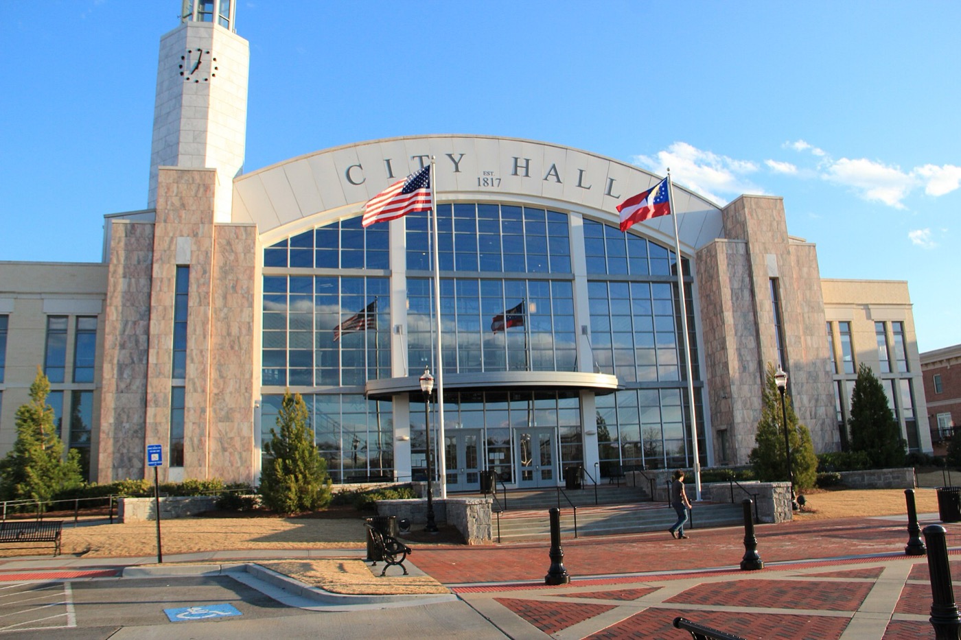 Suwanee City Hall with a clock tower and glass front, seen from the brick plaza