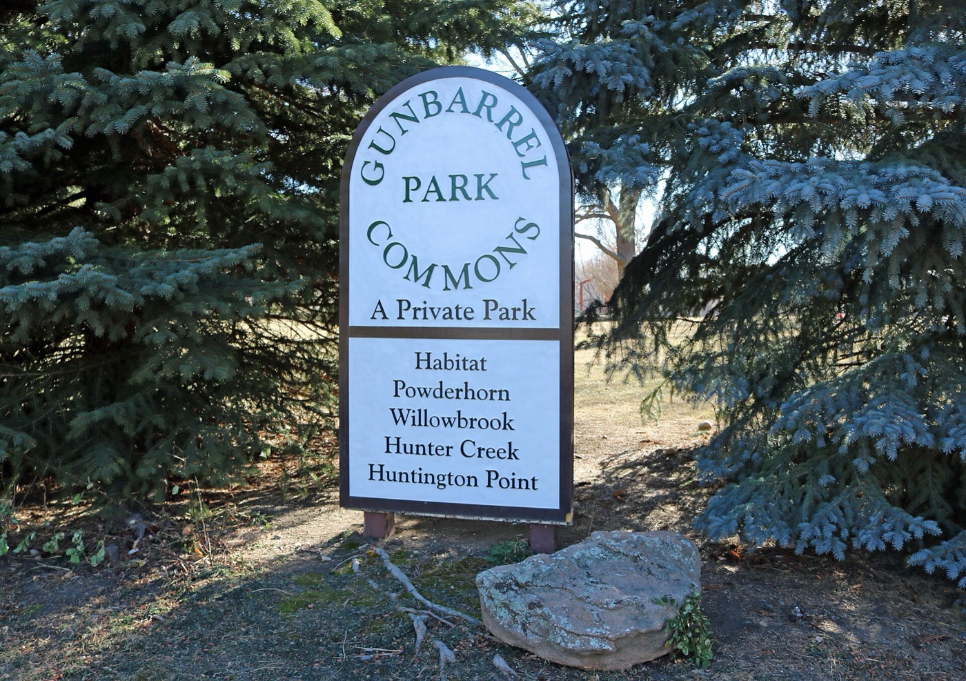 Gunbarrel Park Commons sign listing local neighborhoods, framed by evergreen trees