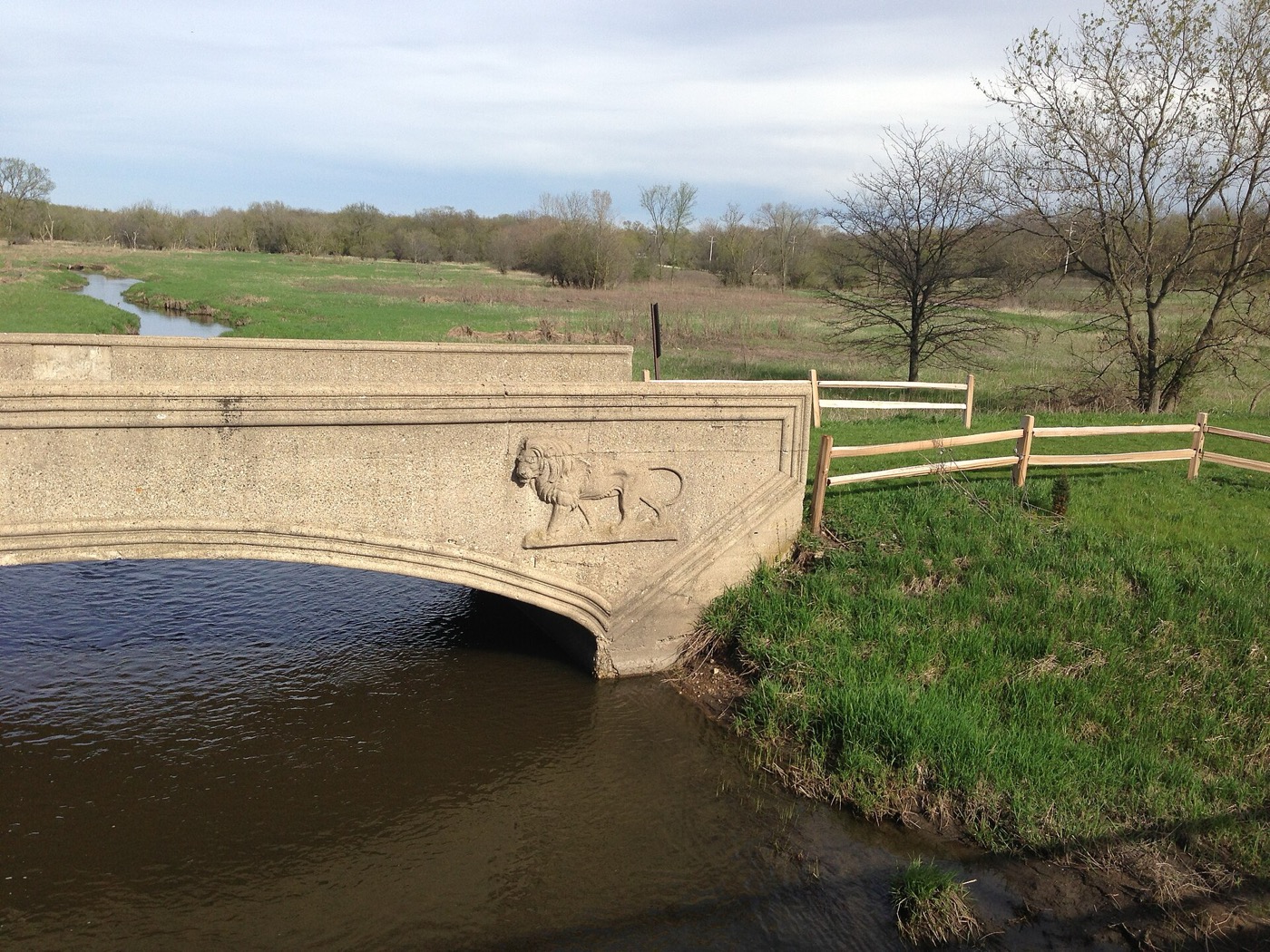 A stone arch bridge with a carved lion relief over a creek in Hoffman Estates