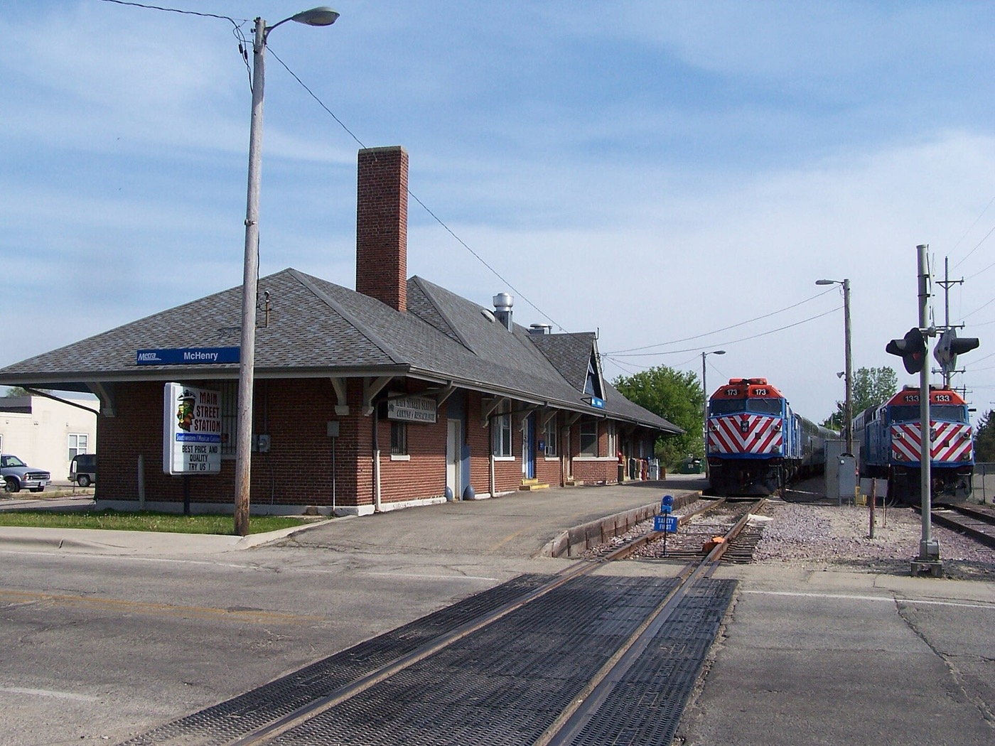 Brick McHenry Metra station building with a commuter train on the tracks