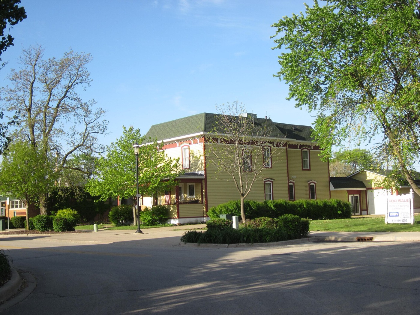 Two-story historic brick building with green trim on a tree-lined street in Plainfield, Illinois