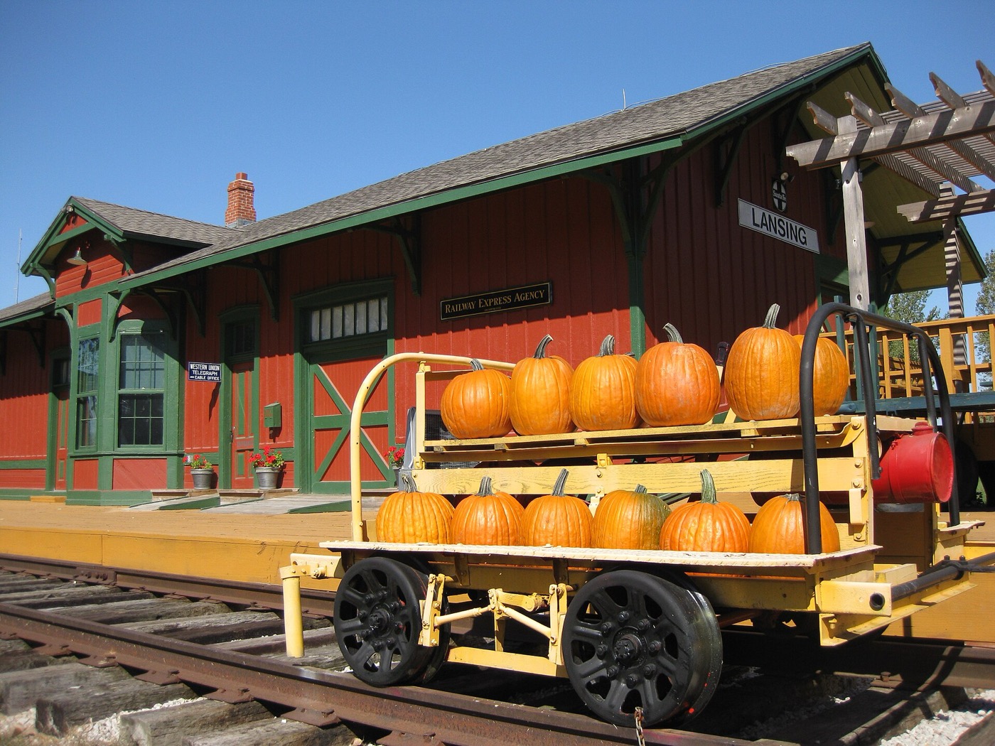 Red and green railroad depot of the Lansing Historical Museum with a rail cart of pumpkins in Lansing, Kansas