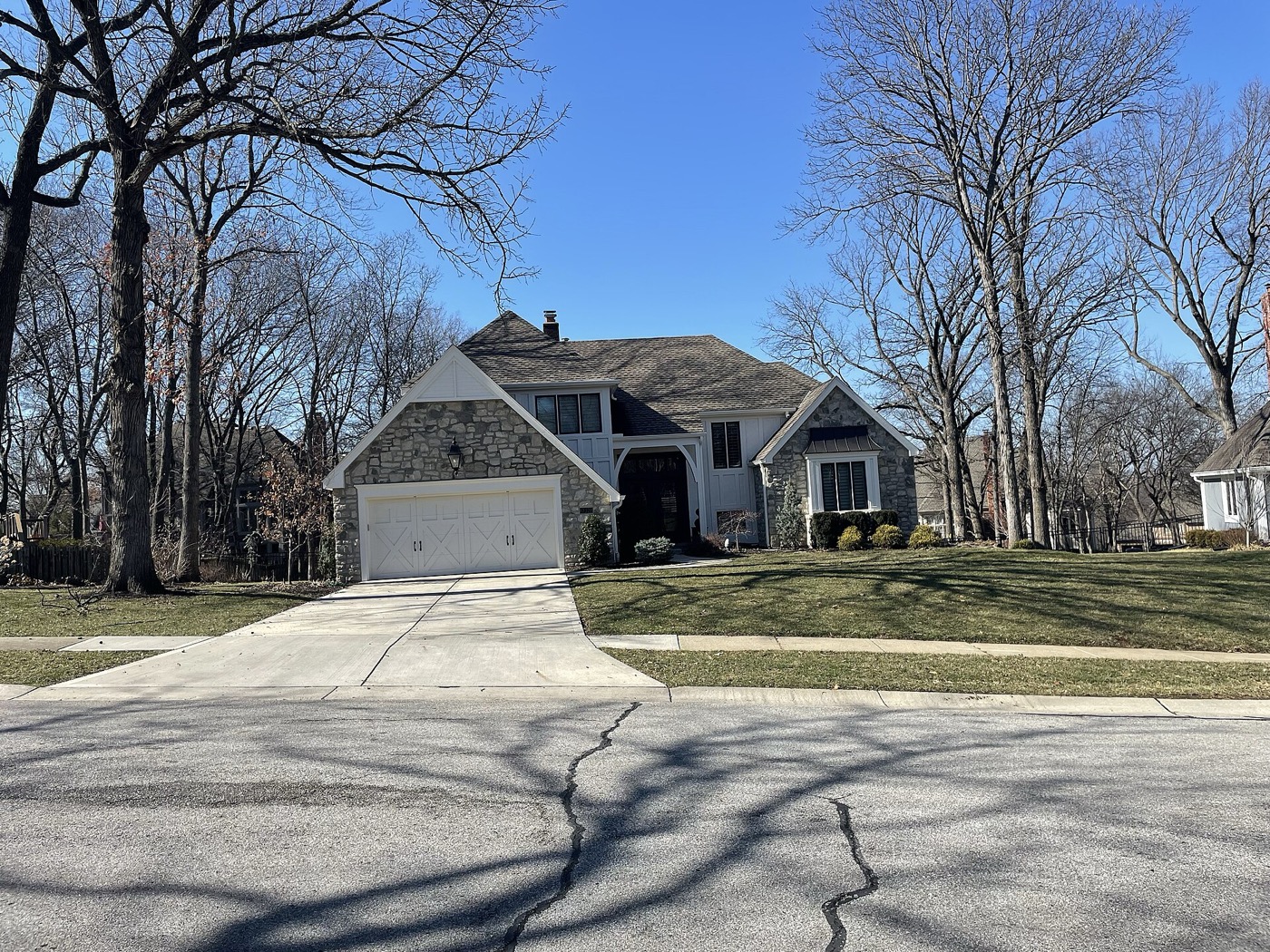 Stone and white-trim two-story house with an attached garage on a tree-lined street in Leawood, Kansas