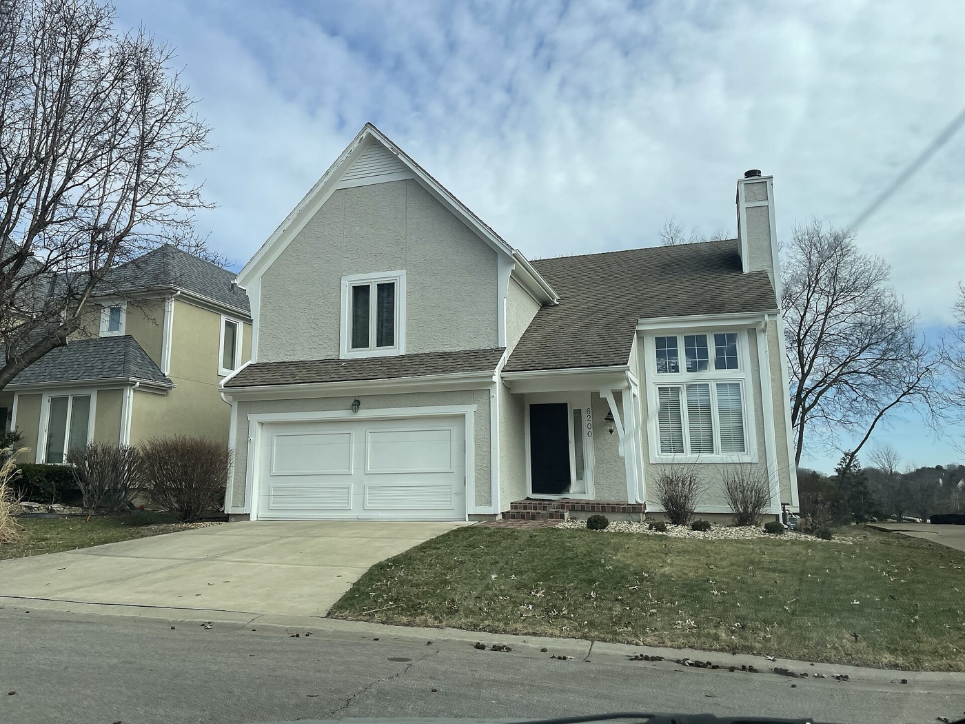 Stucco two-story house with a white two-car garage door on a residential street in Overland Park, Kansas