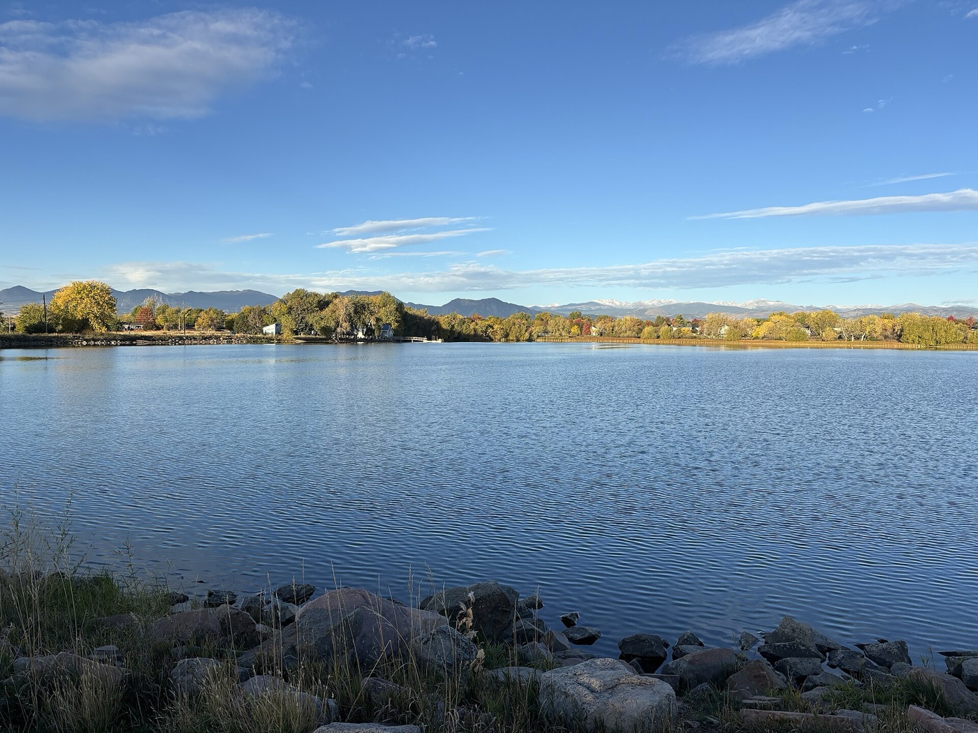 Calm blue Waneka Lake in Lafayette with autumn trees and the Front Range beyond