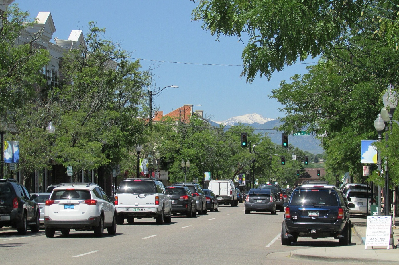 Historic downtown Littleton Main Street with parked cars, trees and mountains in the distance