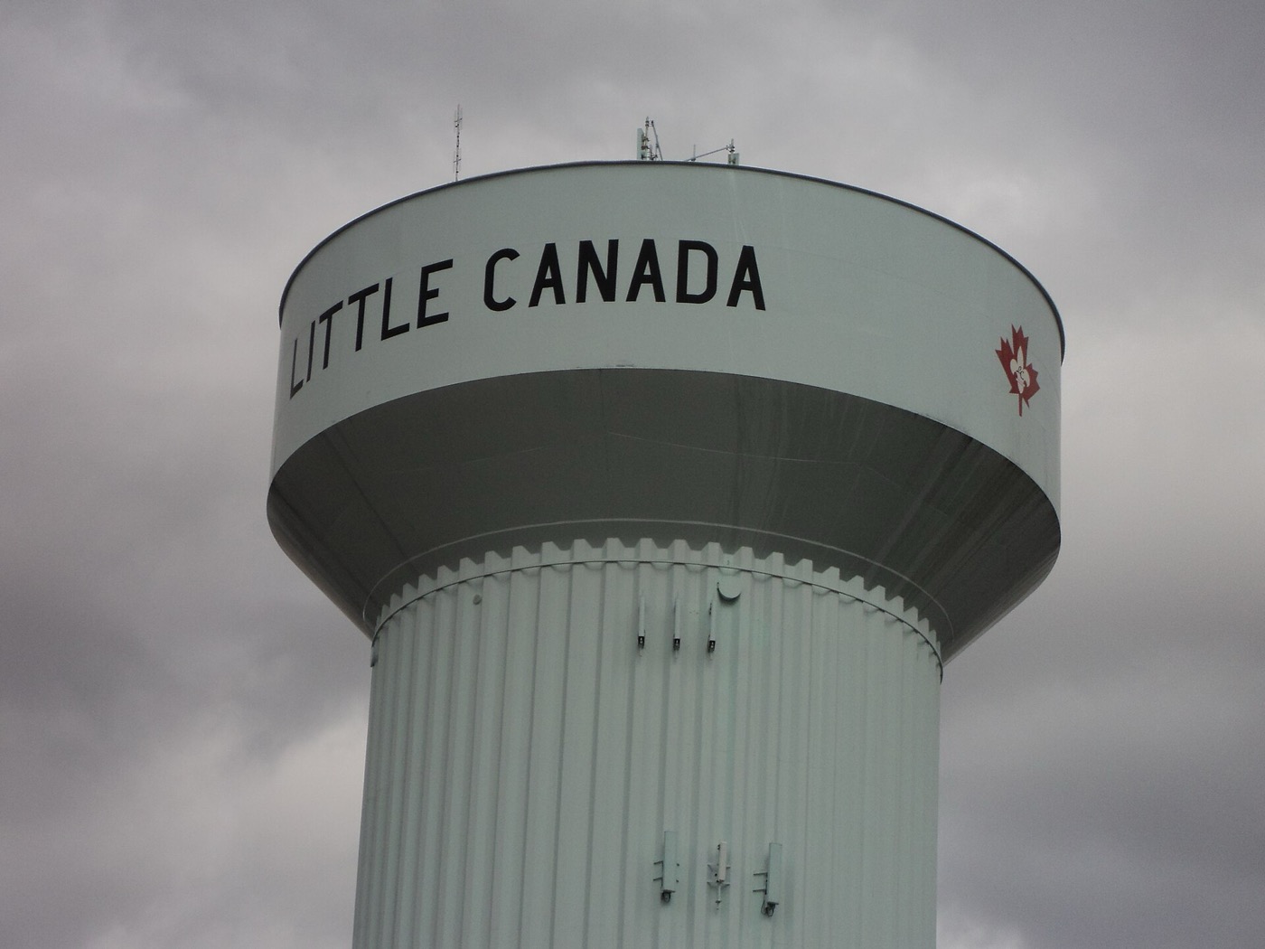 Pale green Little Canada water tower with a red maple leaf emblem against a cloudy sky