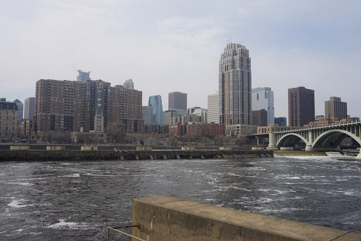 Downtown Minneapolis high-rises behind the Mississippi River and an arched bridge