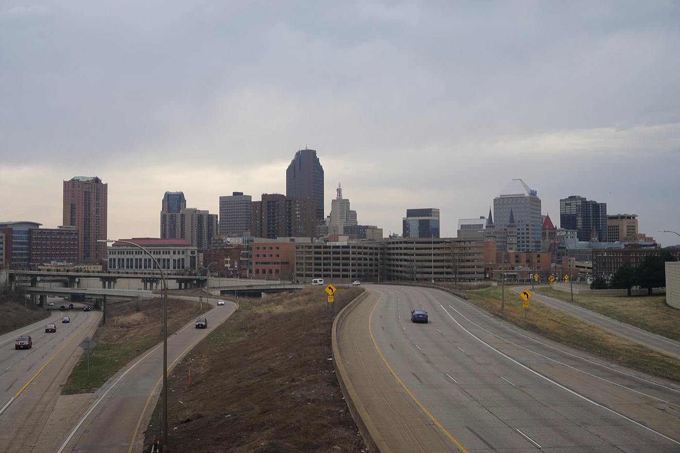 Downtown Saint Paul office towers seen from a highway overpass under a cloudy sky