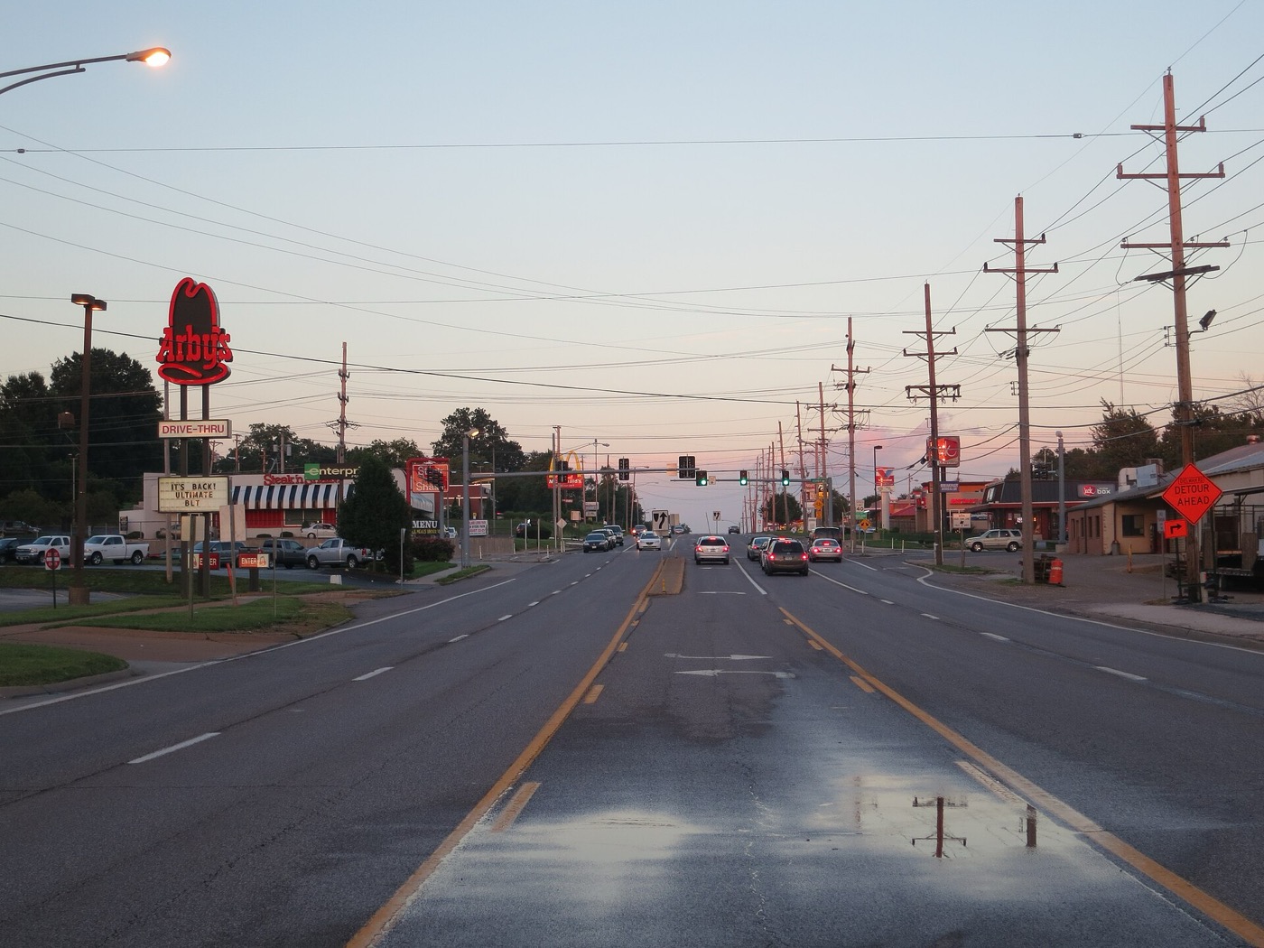 Wide suburban arterial road lined with utility poles and roadside businesses at dusk in Maryland Heights, Missouri