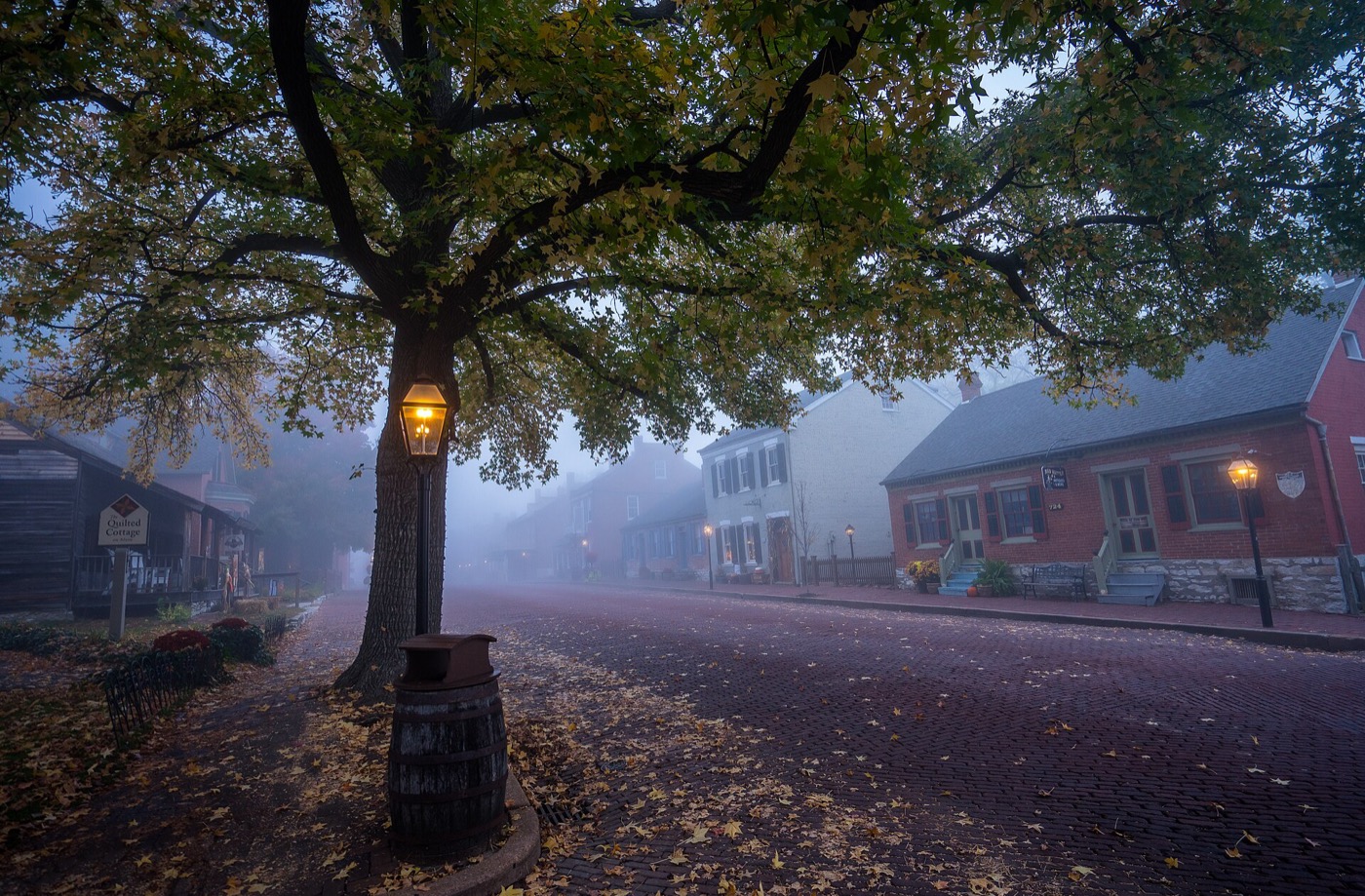Brick buildings, a gas lamp and autumn leaves on a misty street in St. Charles, Missouri