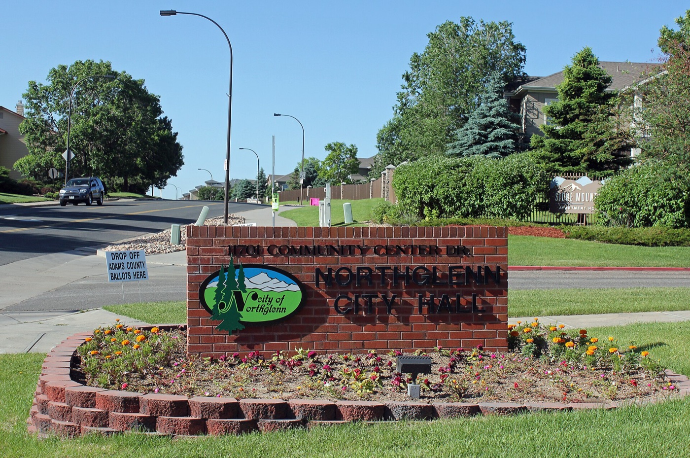 Brick Northglenn City Hall sign with flower bed along a residential street with trees