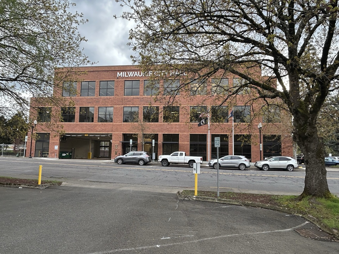 Brick Milwaukie City Hall building behind a parking lot and a large tree